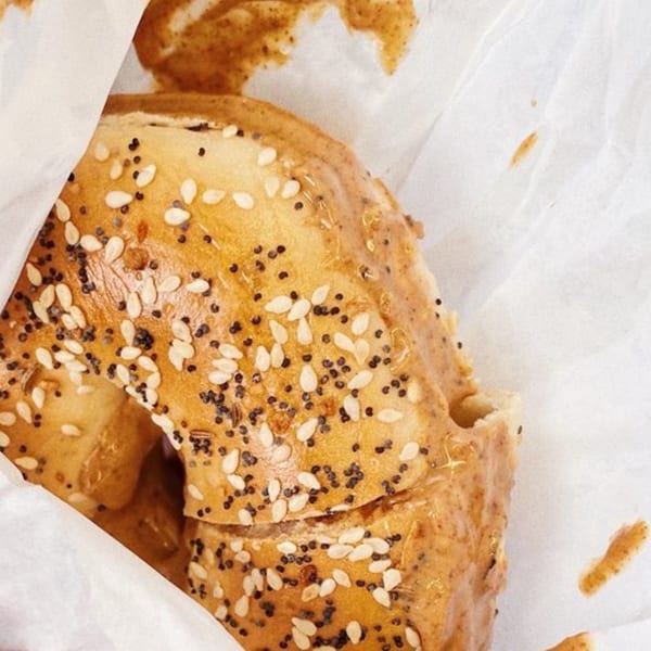 Close-up of a sesame and poppy seed bagel with peanut butter, wrapped in white paper.