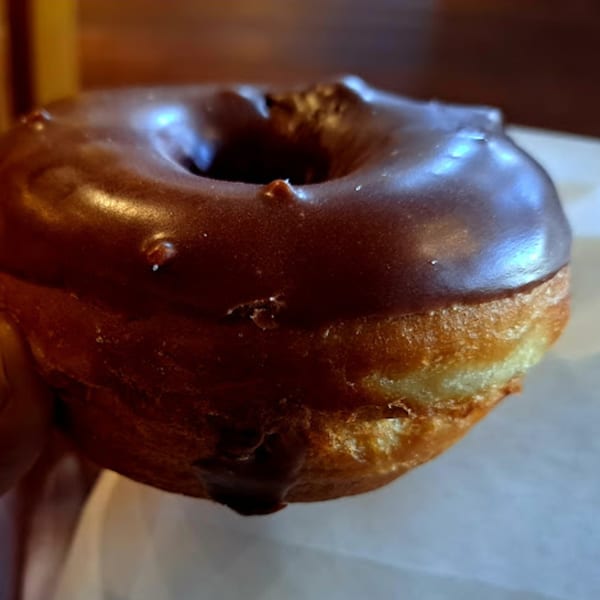 A close-up of a chocolate-glazed donut from Java Beach cafe, with a rich, dark frosting.