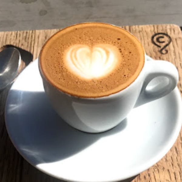 A cup of Java Beach latte with heart-shaped latte art on a wooden table.