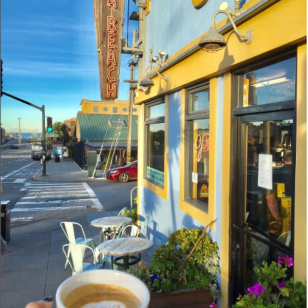 A latte with foam art in the foreground, with Java Beach cafe and outdoor seating in the background.