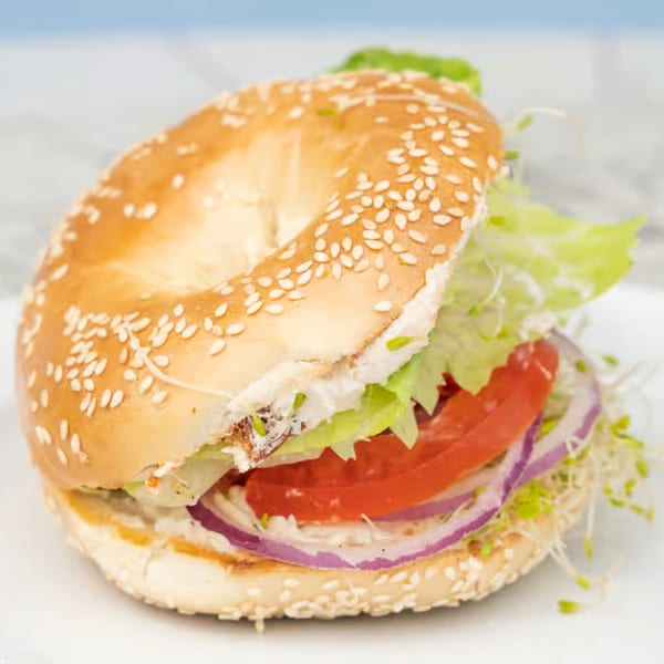 A sesame seed bagel sandwich from Java Beach, filled with lettuce, tomato, red onion, and sprouts.
