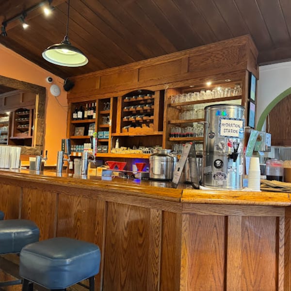A wooden bar with stools, shelves of bottles and glasses, and a "Hydration Station" at Java Beach.