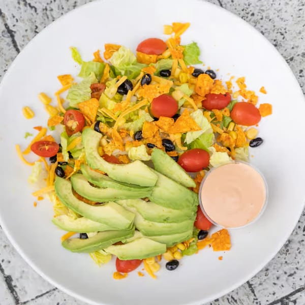 A vibrant taco salad with avocado, cherry tomatoes, black beans, corn, cheese, and tortilla chips.