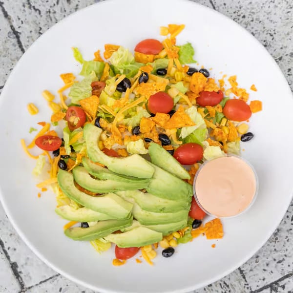 Overhead view of a vibrant taco salad with avocado, tomatoes, corn, black beans, and dressing.