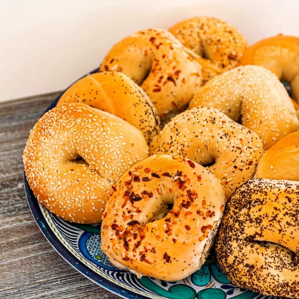 Assortment of fresh bagels with various toppings like sesame, poppy, and everything, on a decorative plate.