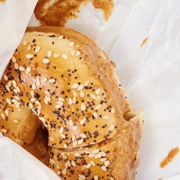 Close-up of a sesame and poppy seed bagel with a smear of cream cheese on white paper.