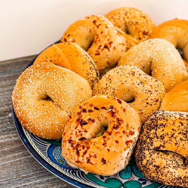 A colorful plate filled with various bagels, including sesame, poppy seed, and everything bagels.