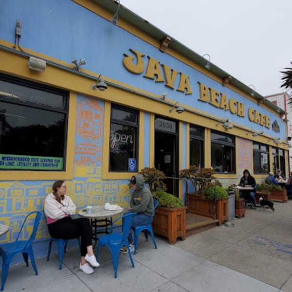 The exterior of Java Beach Cafe, a blue and yellow building with outdoor seating and patrons.