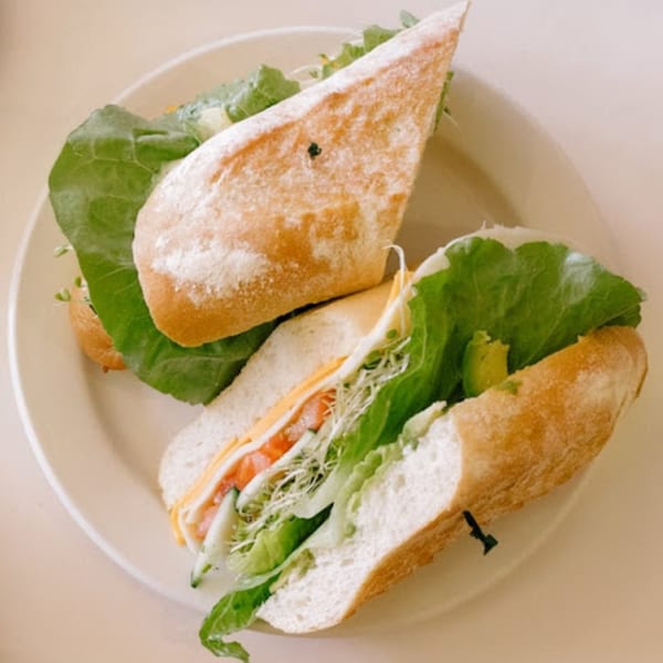 Two fresh sandwiches on a white plate, filled with lettuce, cheese, tomatoes, and sprouts.