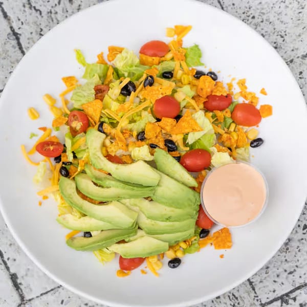 A vibrant taco salad with avocado, cherry tomatoes, black beans, corn, and tortilla chips.