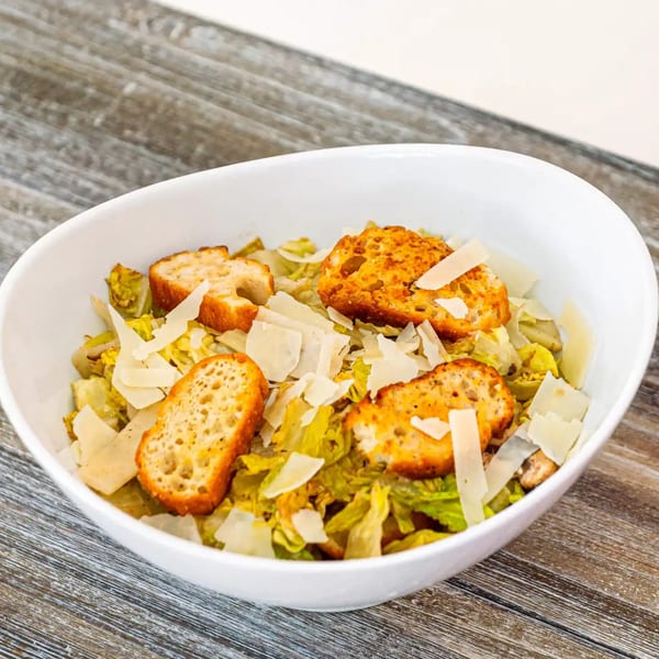 Caesar salad with crisp romaine lettuce, large croutons, and shaved Parmesan cheese in a white bowl.