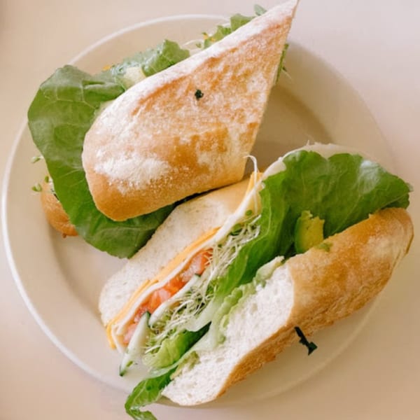 Two fresh sandwiches on a white plate, filled with lettuce, cheese, tomato, and sprouts.
