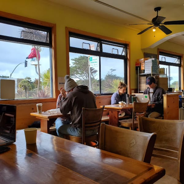 Customers enjoying coffee and working on laptops inside Java Beach cafe with large windows overlooking the street.