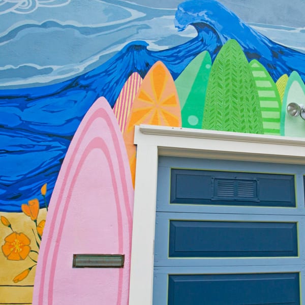 A vibrant mural of surfboards and ocean waves next to a blue garage door at Java Beach.