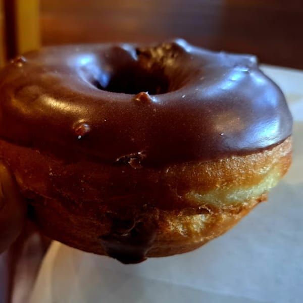 A close-up of a chocolate-glazed donut from Java Beach, with a rich brown frosting.