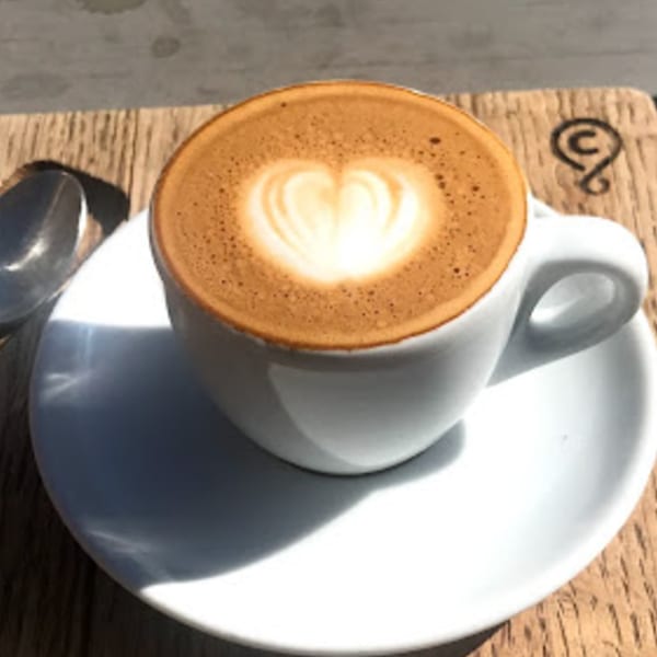 A cup of Java Beach latte with heart-shaped latte art on a wooden table.
