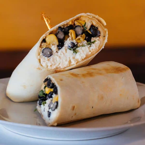 Two Java Beach burritos, one cut in half, revealing black beans, corn, and white cheese filling.