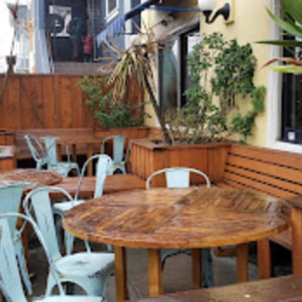 Java Beach cafe's outdoor patio with wooden tables, light blue chairs, and planters.
