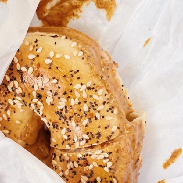 Close-up of a Java Beach everything bagel with sesame and poppy seeds, wrapped in white paper.