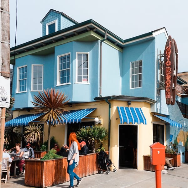 The vibrant blue and yellow exterior of Java Beach cafe with striped awnings and outdoor seating.