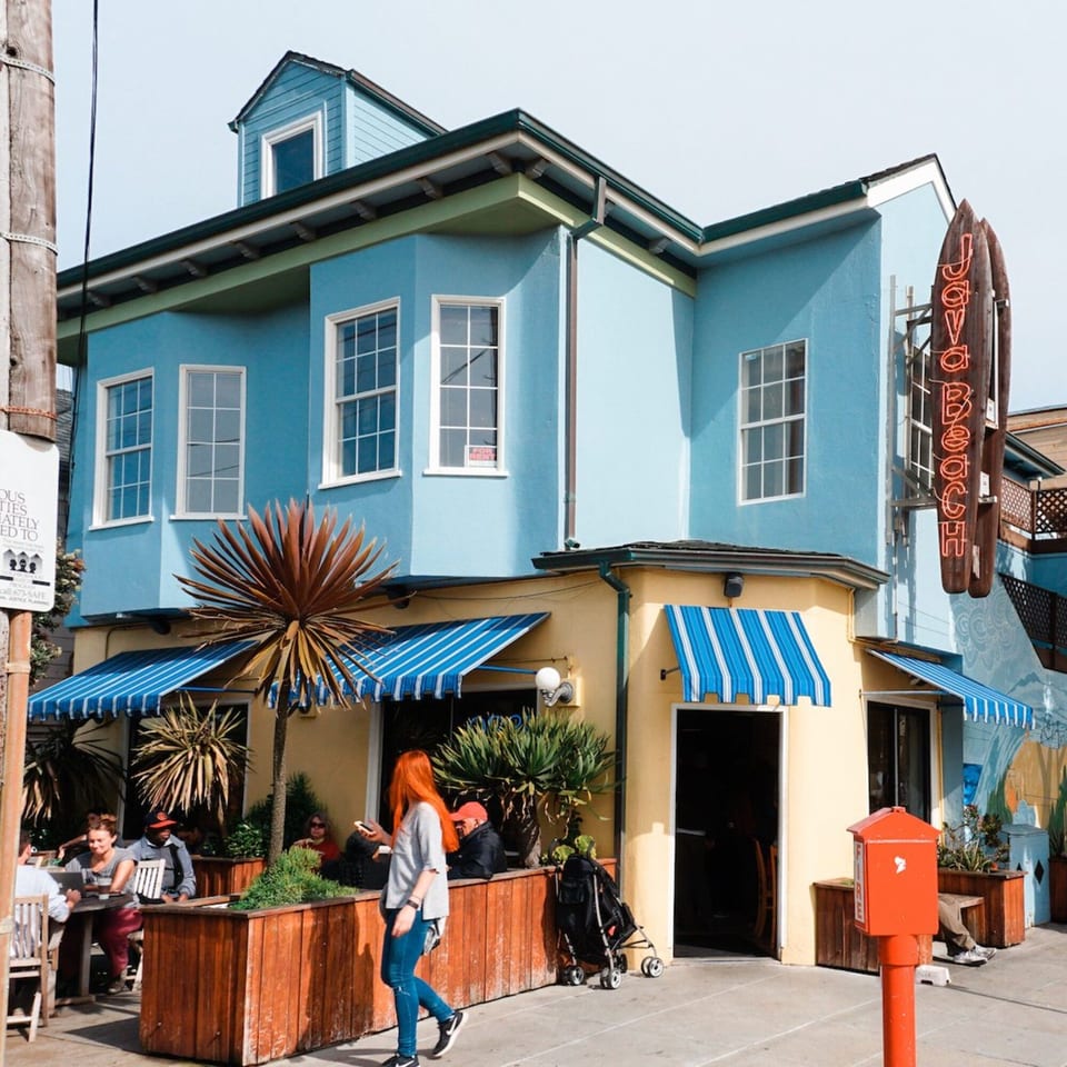 The vibrant blue and yellow exterior of Java Beach cafe with striped awnings and outdoor seating.