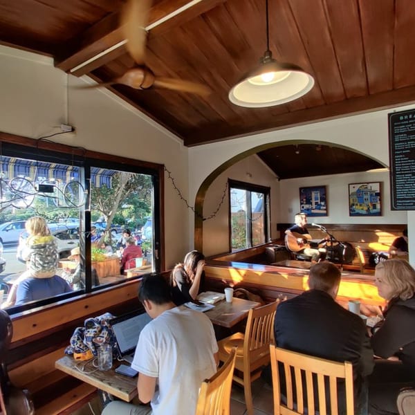 Inside Java Beach cafe, people sit at tables and a musician plays guitar on a small stage.