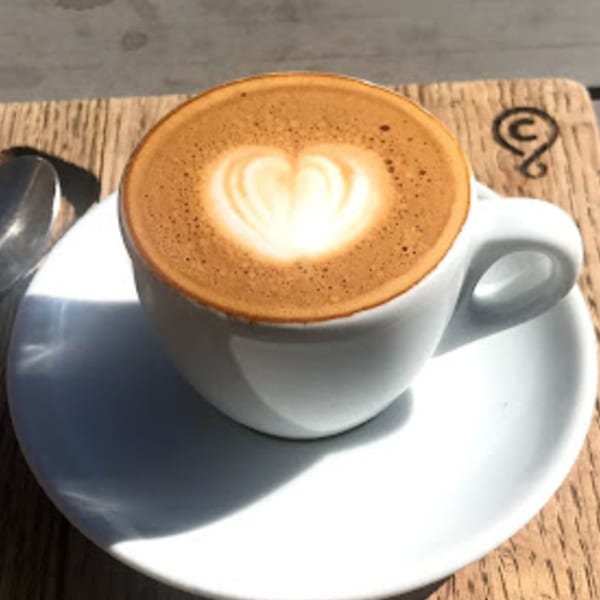 A white cup of Java Beach latte with heart-shaped foam art on a wooden table.