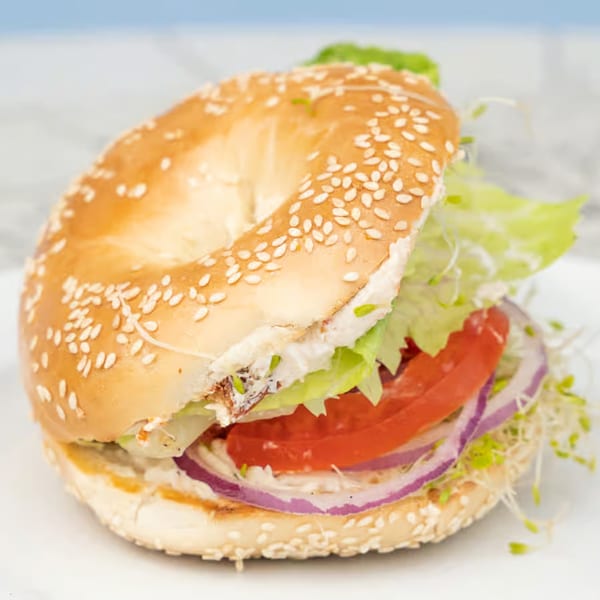 A sesame seed bagel sandwich with lettuce, tomato, red onion, and sprouts on a white plate.